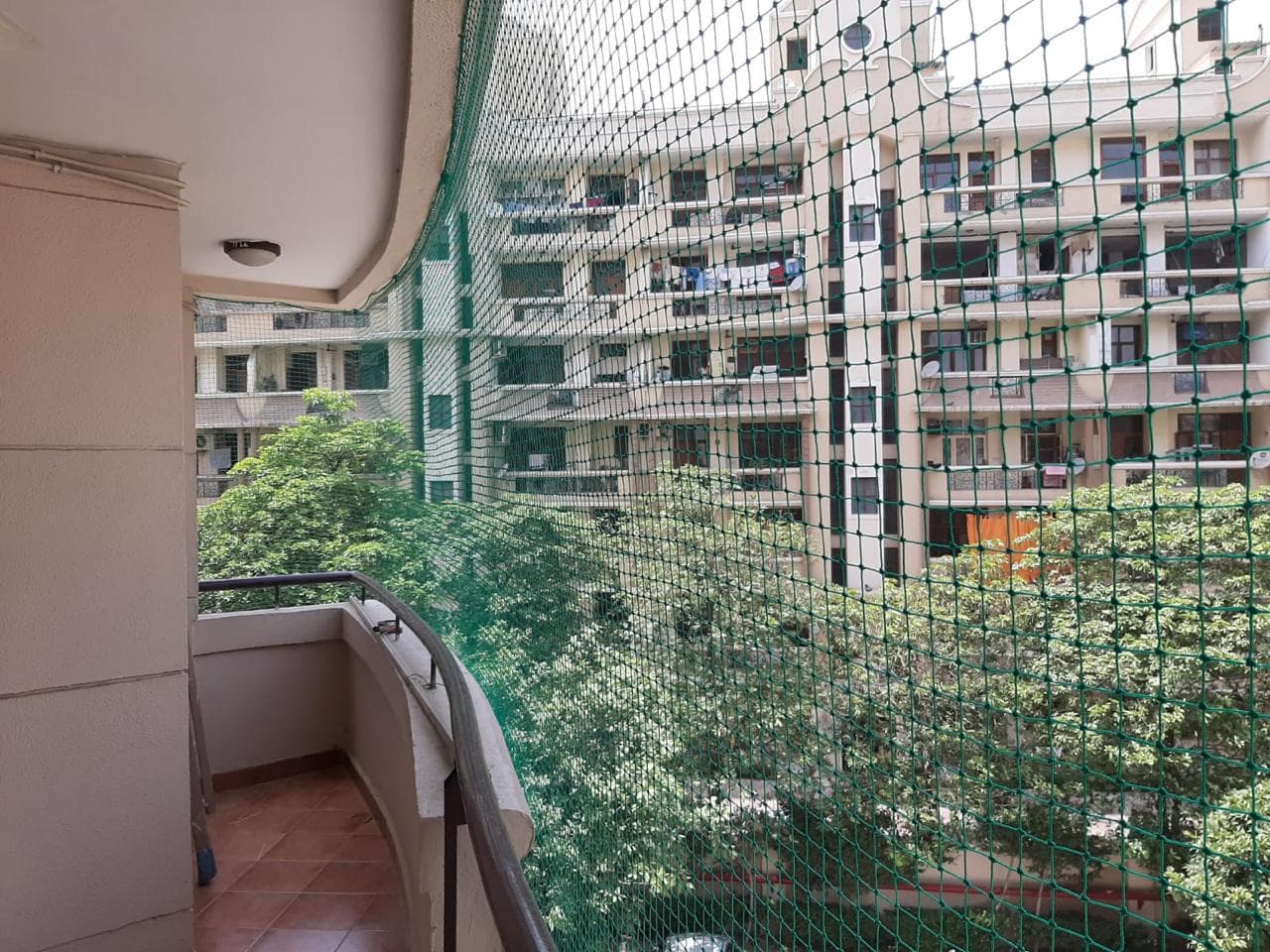 Green square-mesh balcony net overlooking a courtyard